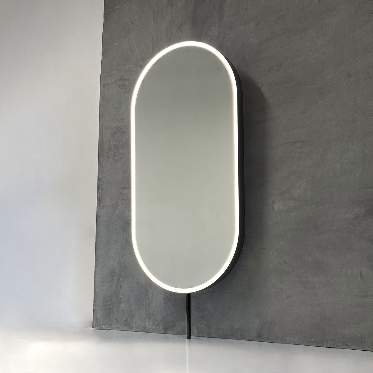 Modern front illuminated countertop pill shaped mirror with a blackened stainless steel frame