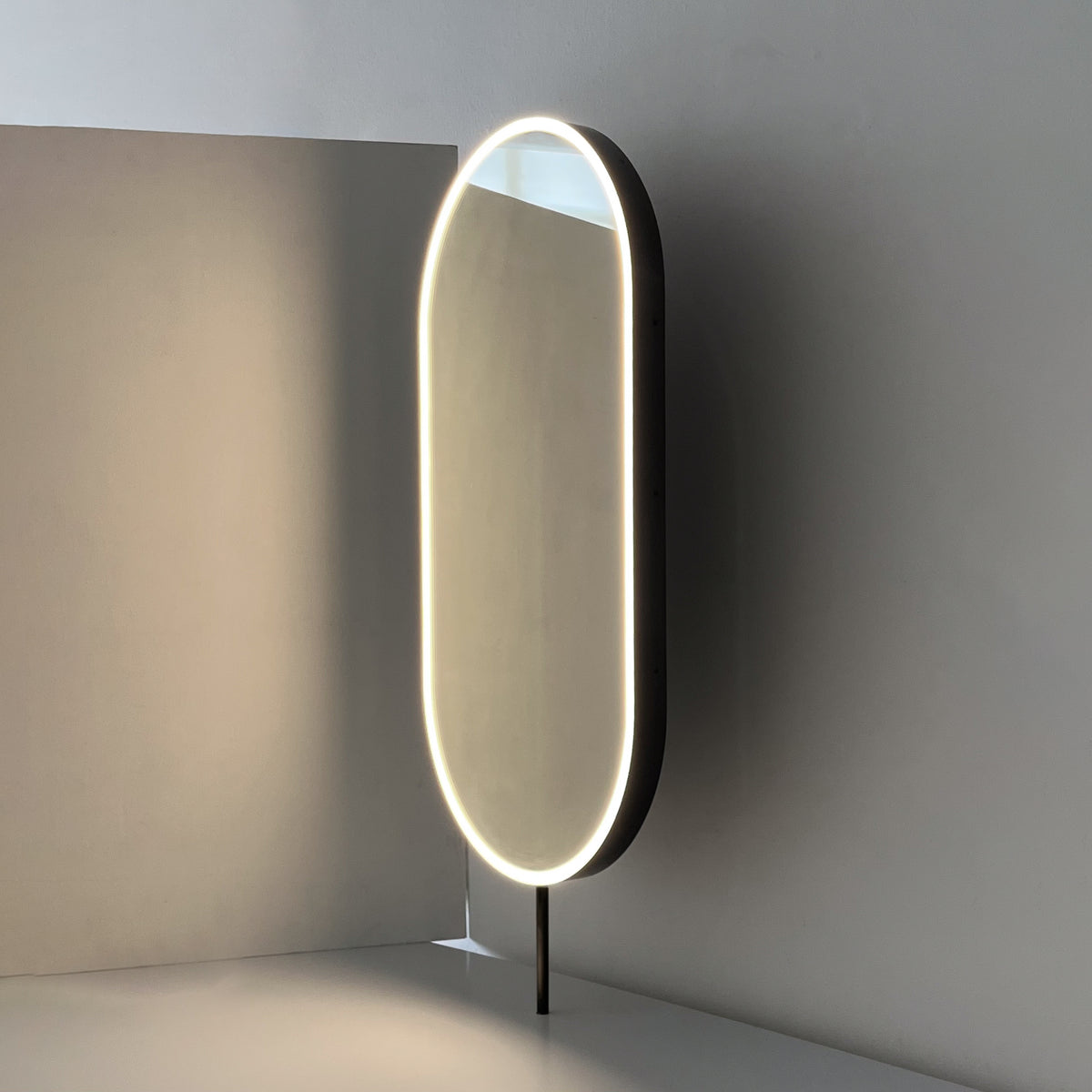 Modern front illuminated countertop pill shaped mirror with a blackened stainless steel frame
