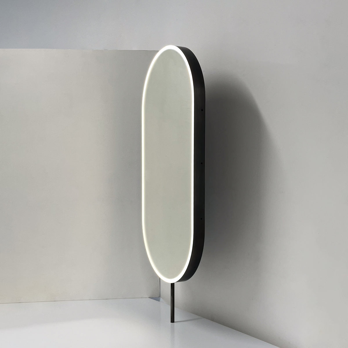 Modern front illuminated countertop pill shaped mirror with a blackened stainless steel frame