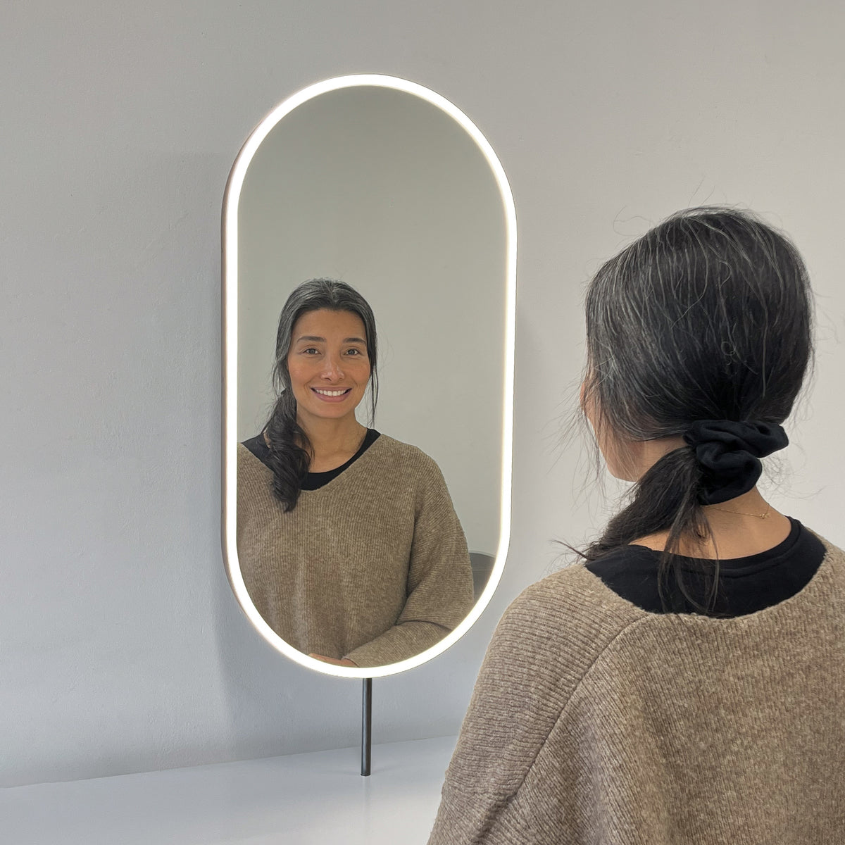 Modern front illuminated countertop pill shaped mirror with a blackened stainless steel frame