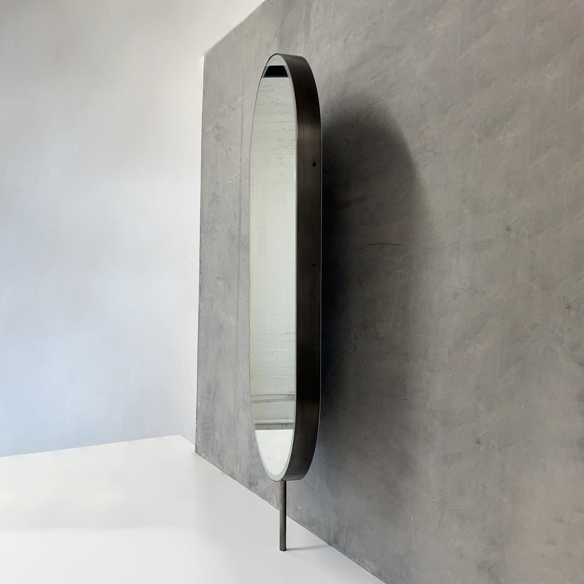 Modern front illuminated countertop pill shaped mirror with a blackened stainless steel frame
