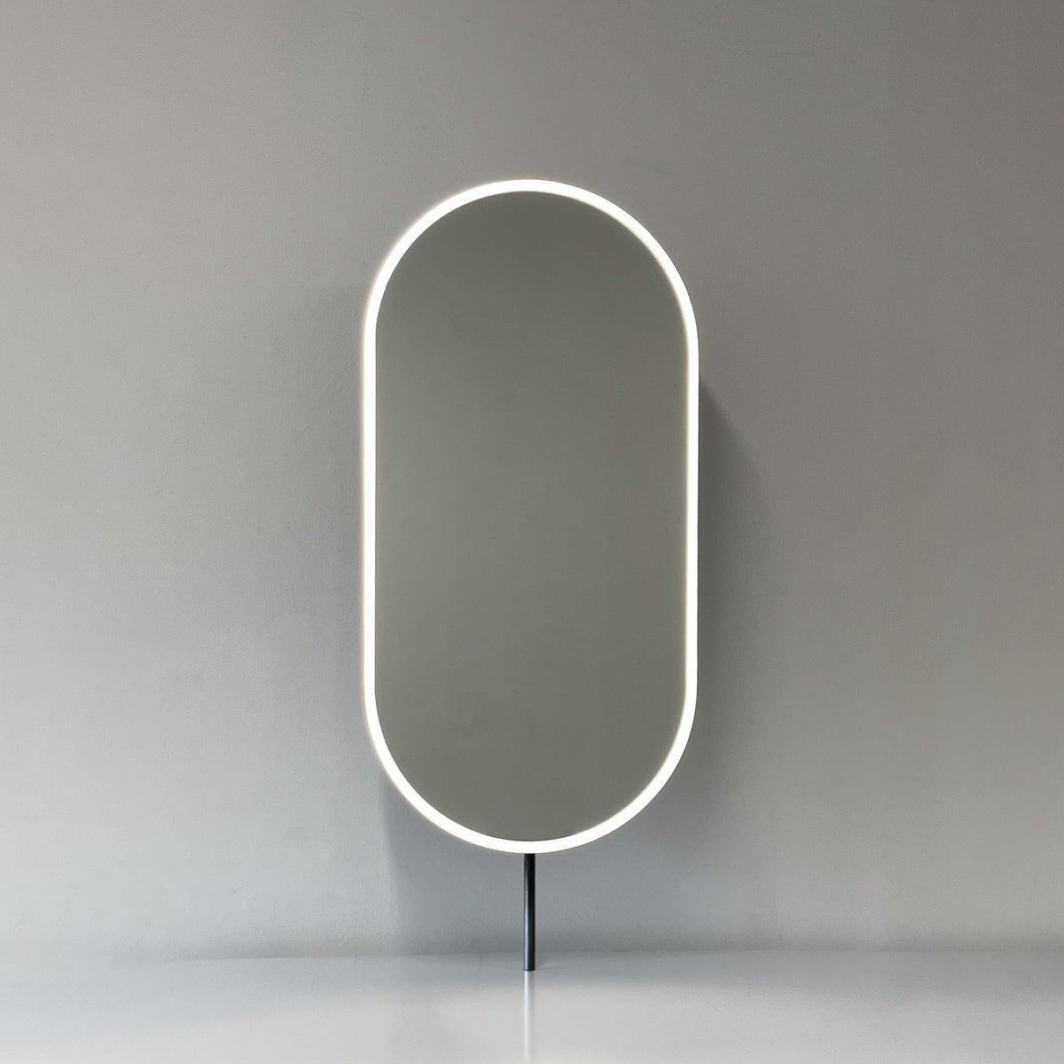 Modern front illuminated countertop pill shaped mirror with a blackened stainless steel frame