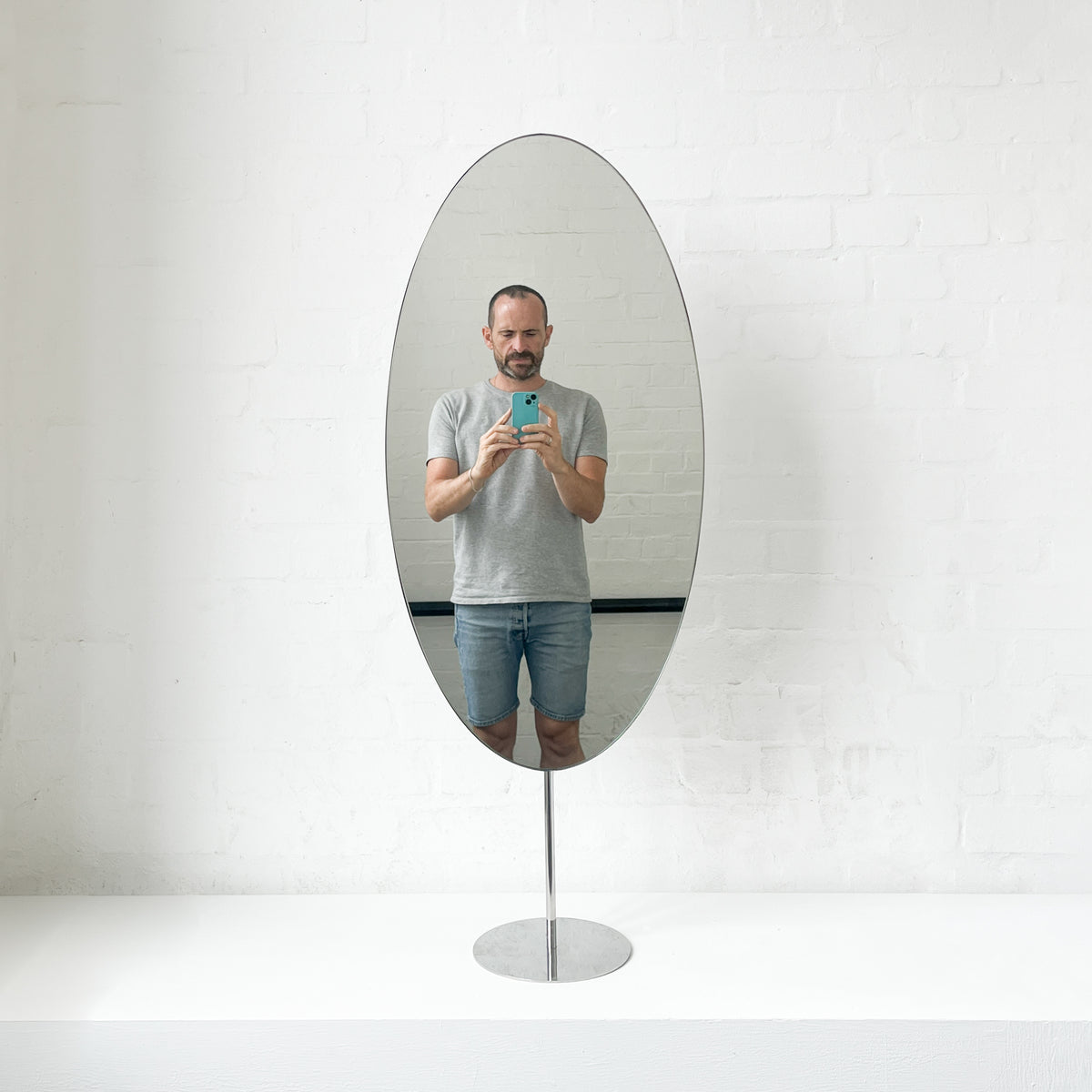 Countertop attached oval mirror with a modern stainless steel frame