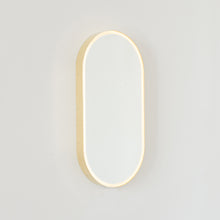 Modern pill shaped mirror with a minimalist brushed brass frame and front illumination