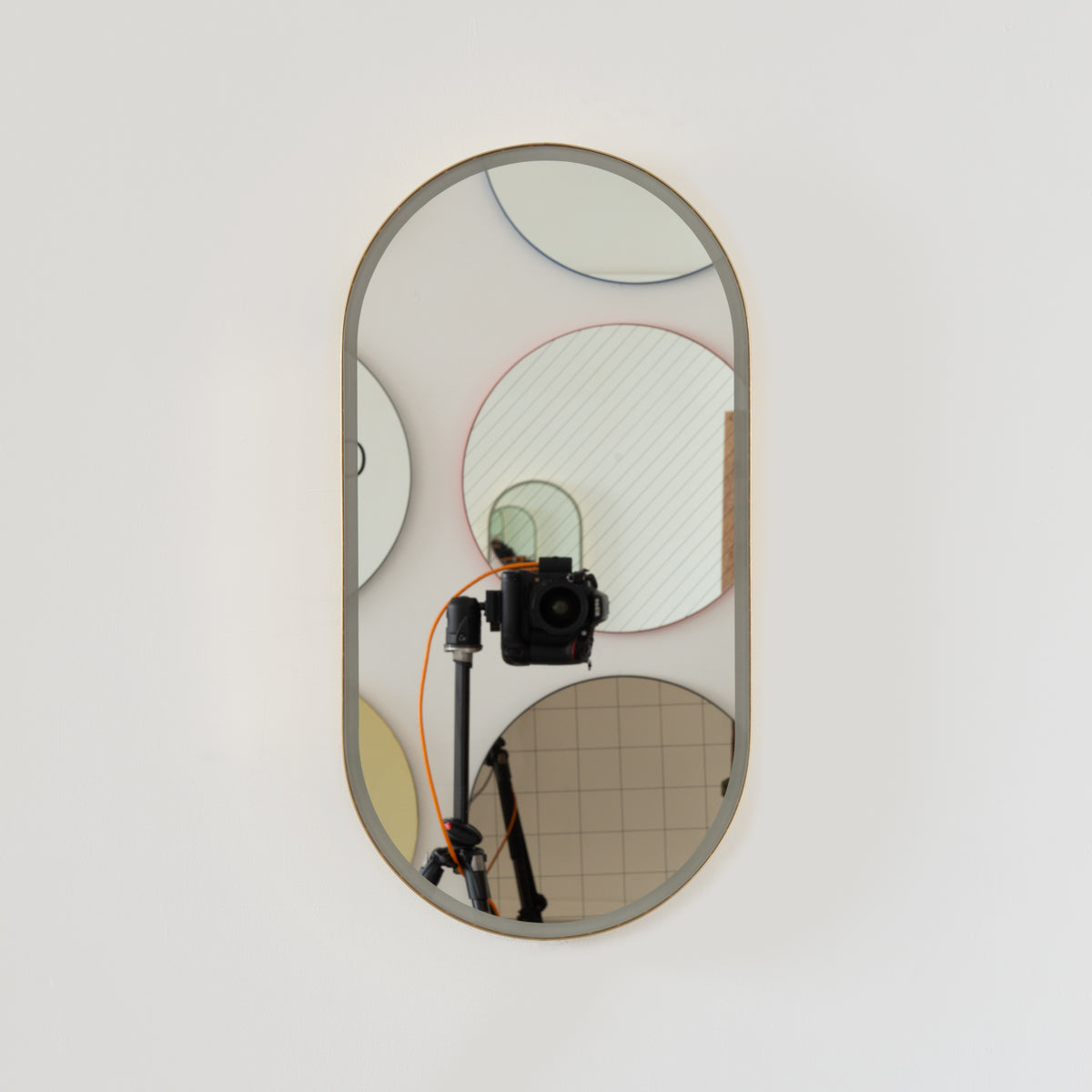 Modern pill shaped Capsula™ mirror with a minimalist solid brass frame and front illumination