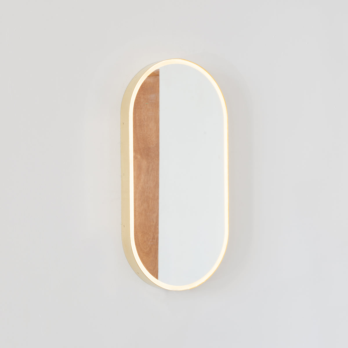 Modern pill shaped Capsula™ mirror with a minimalist solid brass frame and front illumination