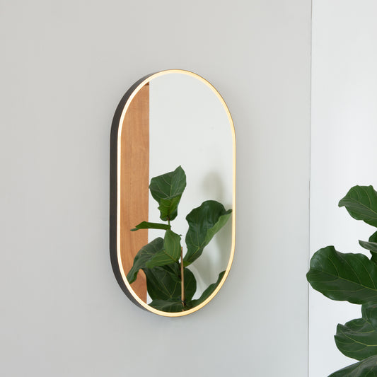 Modern pill shaped mirror with an elegant bronze patina brass frame and front illumination